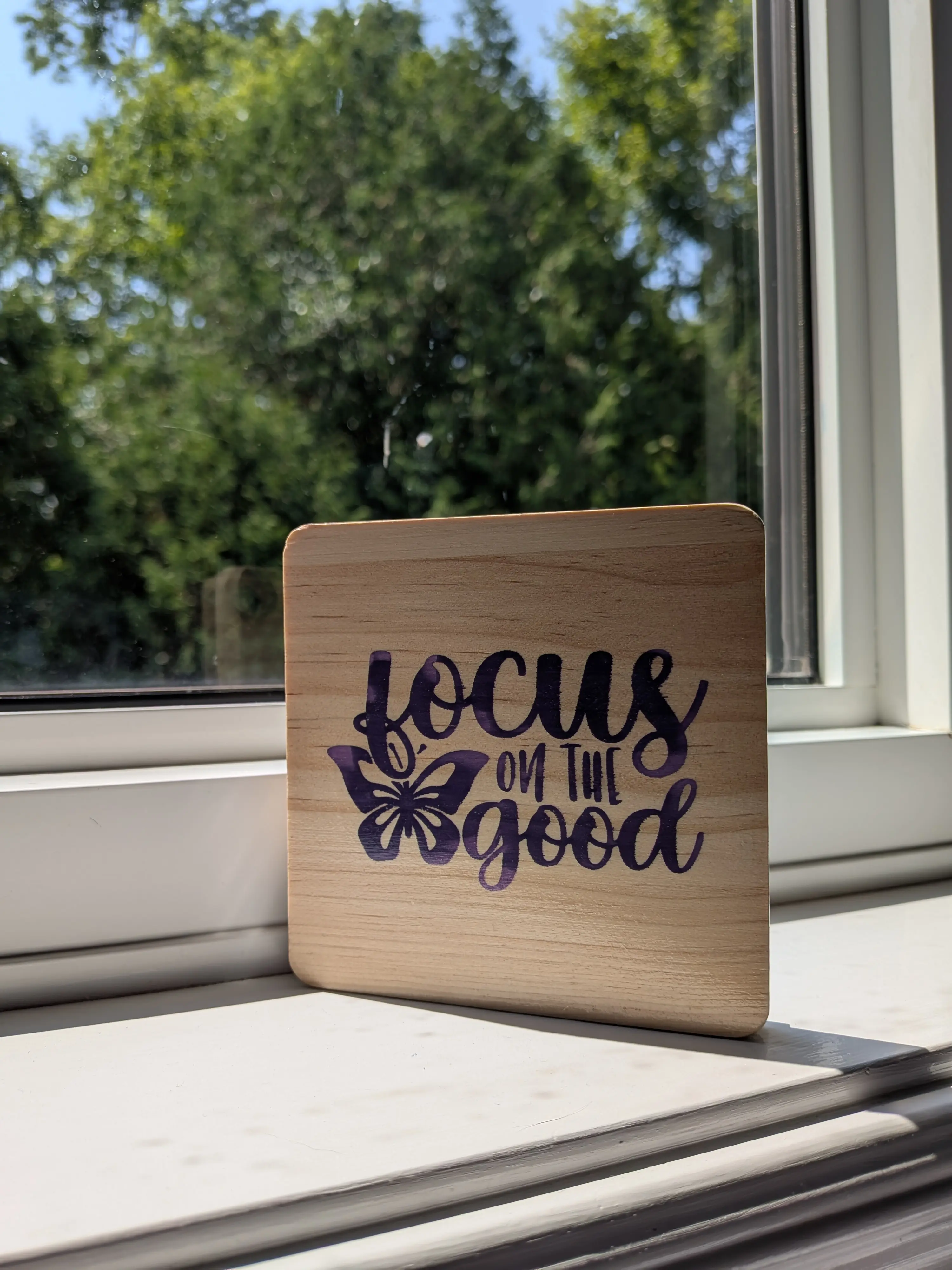 A Coaster which reads 'focus on the good,' placed in front of a window.
